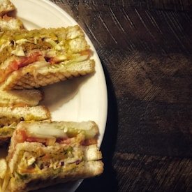 Triangular veggie club sandwiches stacked on a white plate over a wooden table