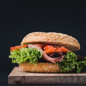 Sandwich with roast beef, lettuce, tomato, and sesame bun on a wooden board