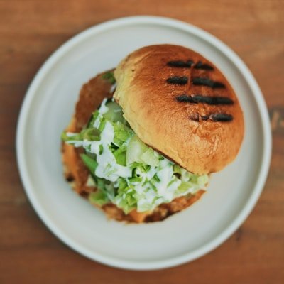 Grilled sandwich with shredded lettuce and sauce on a toasted bun served on a white plate
