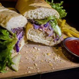 Fresh sub sandwich with lettuce and purple cabbage on a wooden board with fries and ketchup